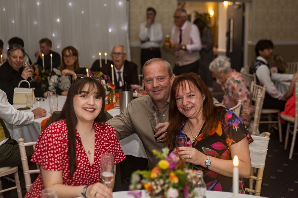 Three guests smile at a candlelit wedding reception dinner table in an elegant venue.