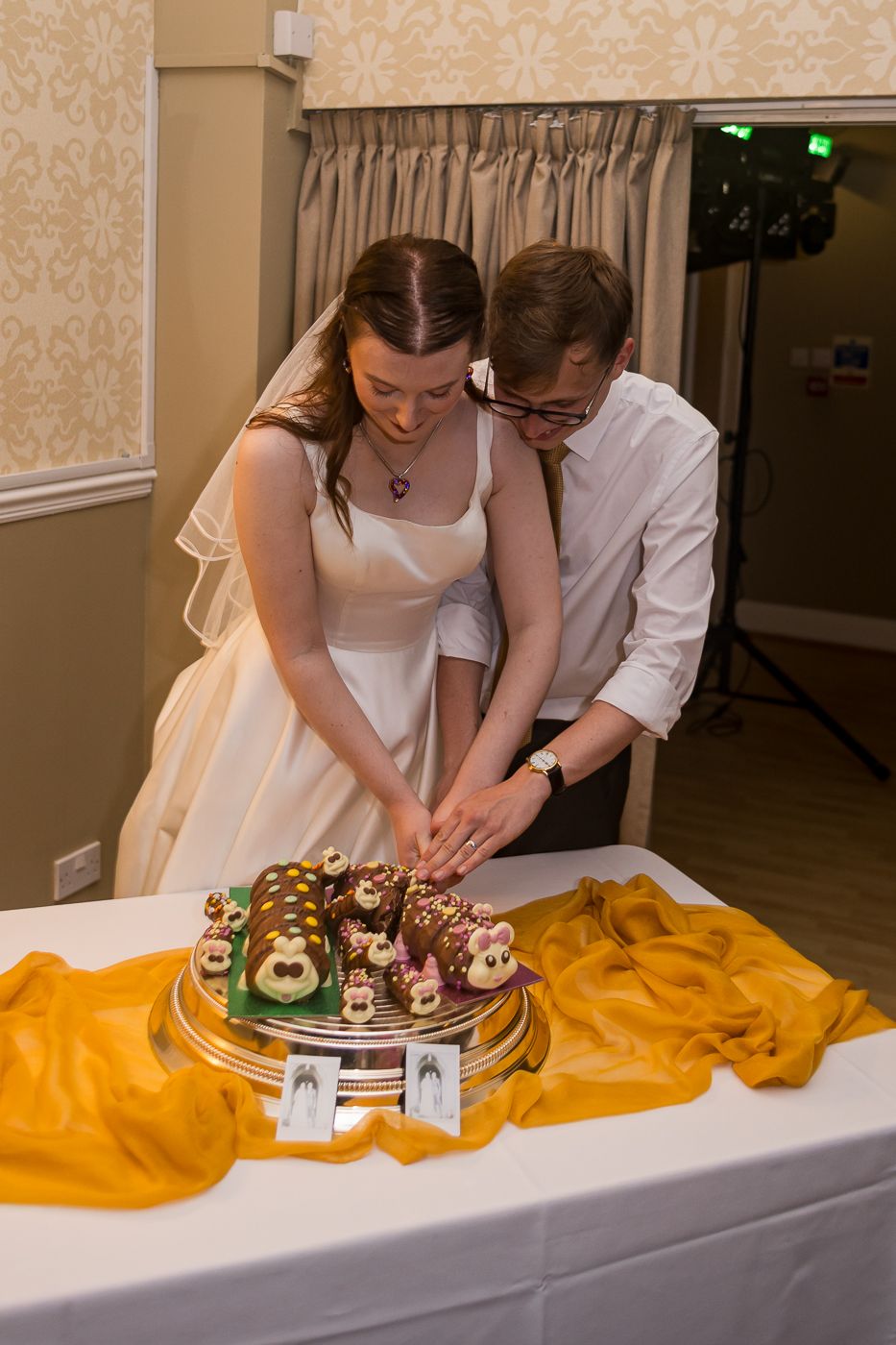 Bride and groom cutting their wedding cake decorated with animal figurines on a gold draped table.