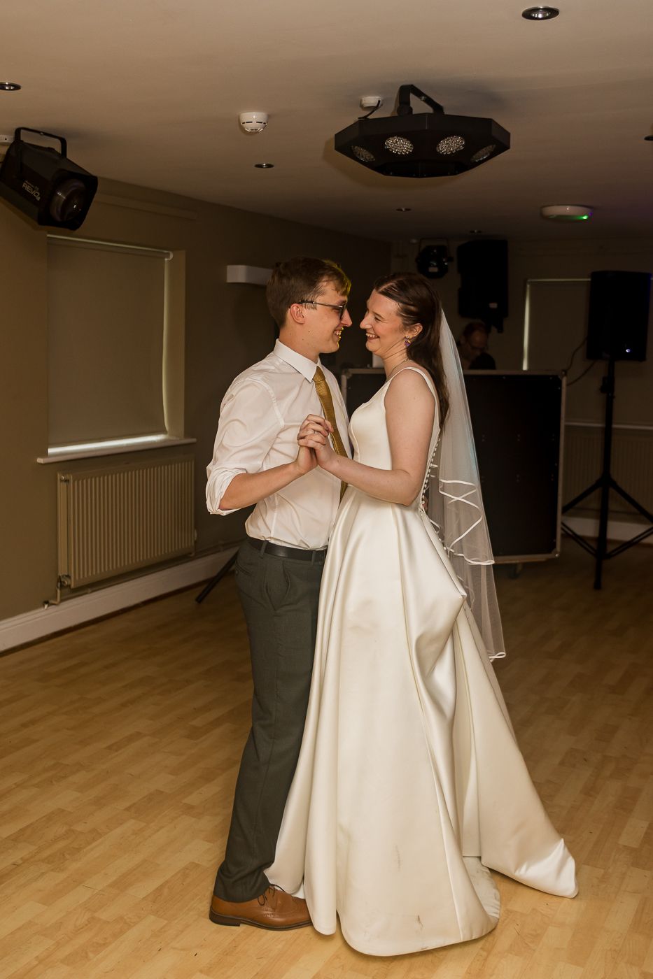 Bride and groom share their first dance in a wedding venue, smiling at each other in formal attire.