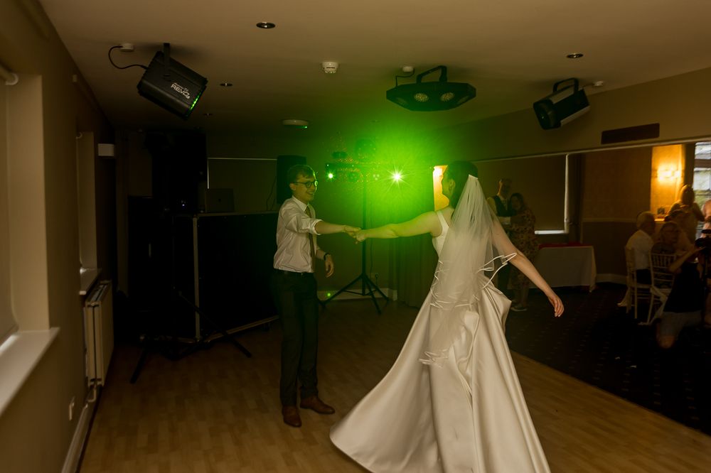 Bride and groom share first dance under green laser lights at wedding reception venue.