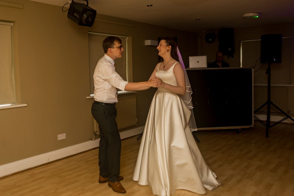 Bride and groom share their first dance at wedding reception, bride wearing elegant white satin gown with veil.