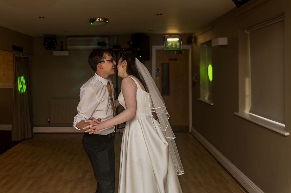 Bride and groom share their first dance in a softly lit wedding reception hall, bride wearing elegant white gown and veil.