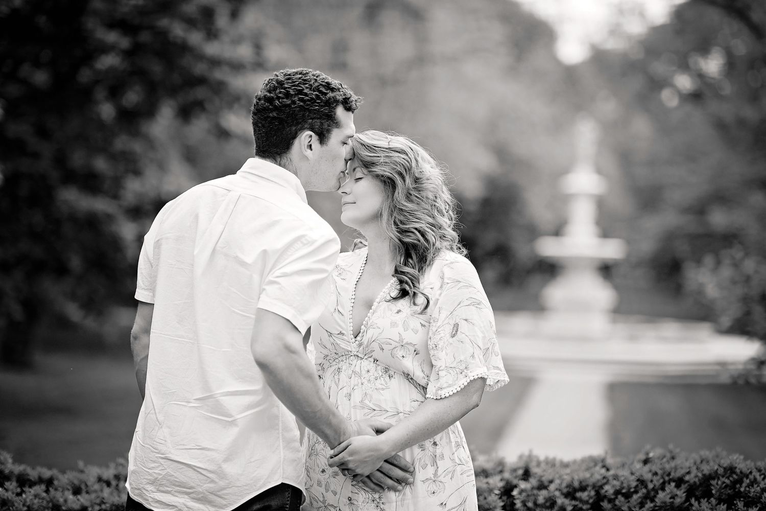 Black and white photo of couple embracing in front of garden fountain.