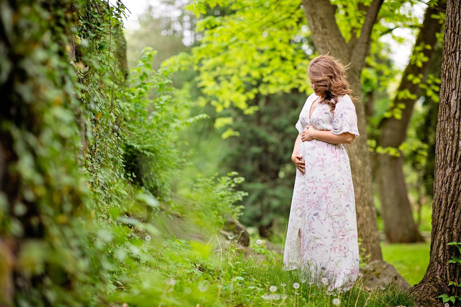 Woman in white lace dress stands thoughtfully in a lush garden setting.