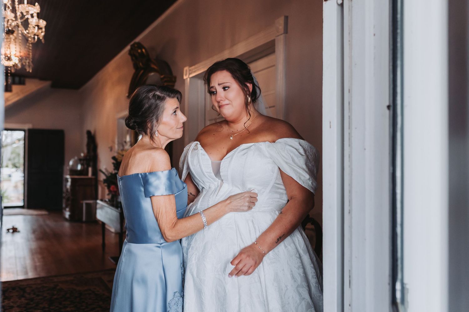 Emotional wedding guests in elegant dresses watch a bride in a lace veil under string lights in a rustic wooden reception venue.