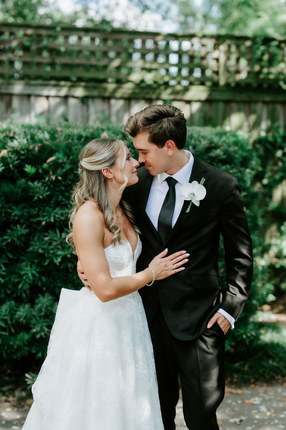 Bride and groom nearly kiss in a garden setting, bride in strapless gown and groom in black suit with white boutonniere.
