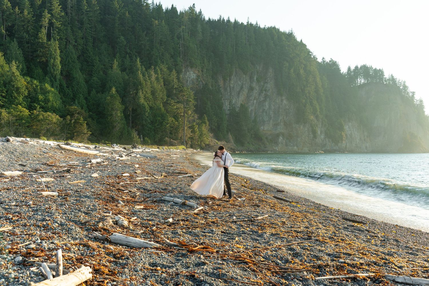 A bride and groom stand together gazing at a stunning mountain landscape surrounded by evergreen trees on their wedding day.