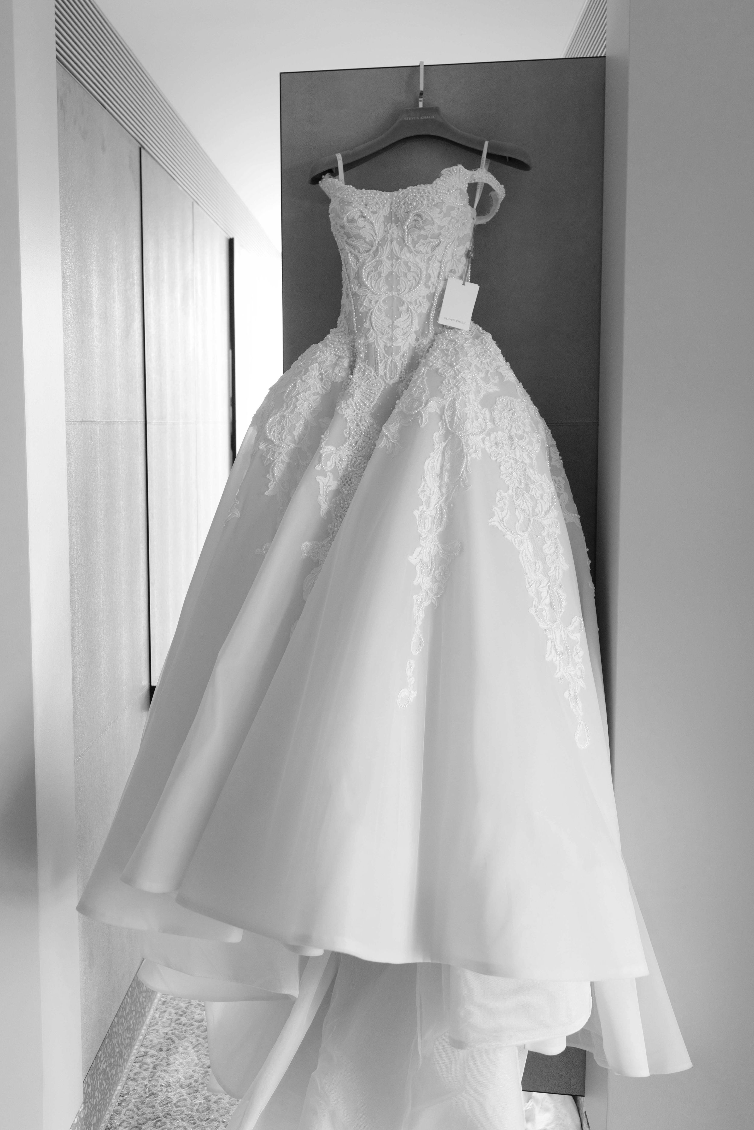 Elegant white ball gown wedding dress with lace bodice hanging on display in black and white photo.