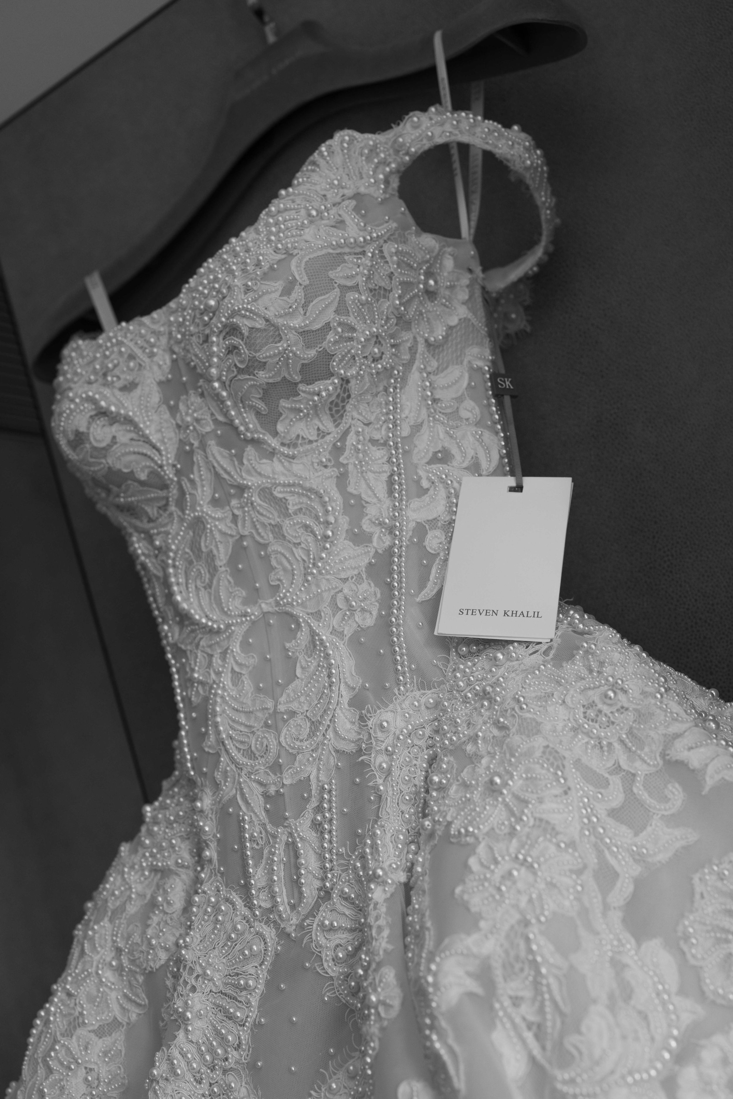 Steven Khalil beaded lace wedding dress on hanger with tags, intricate pearl embellishments, black and white photo.
