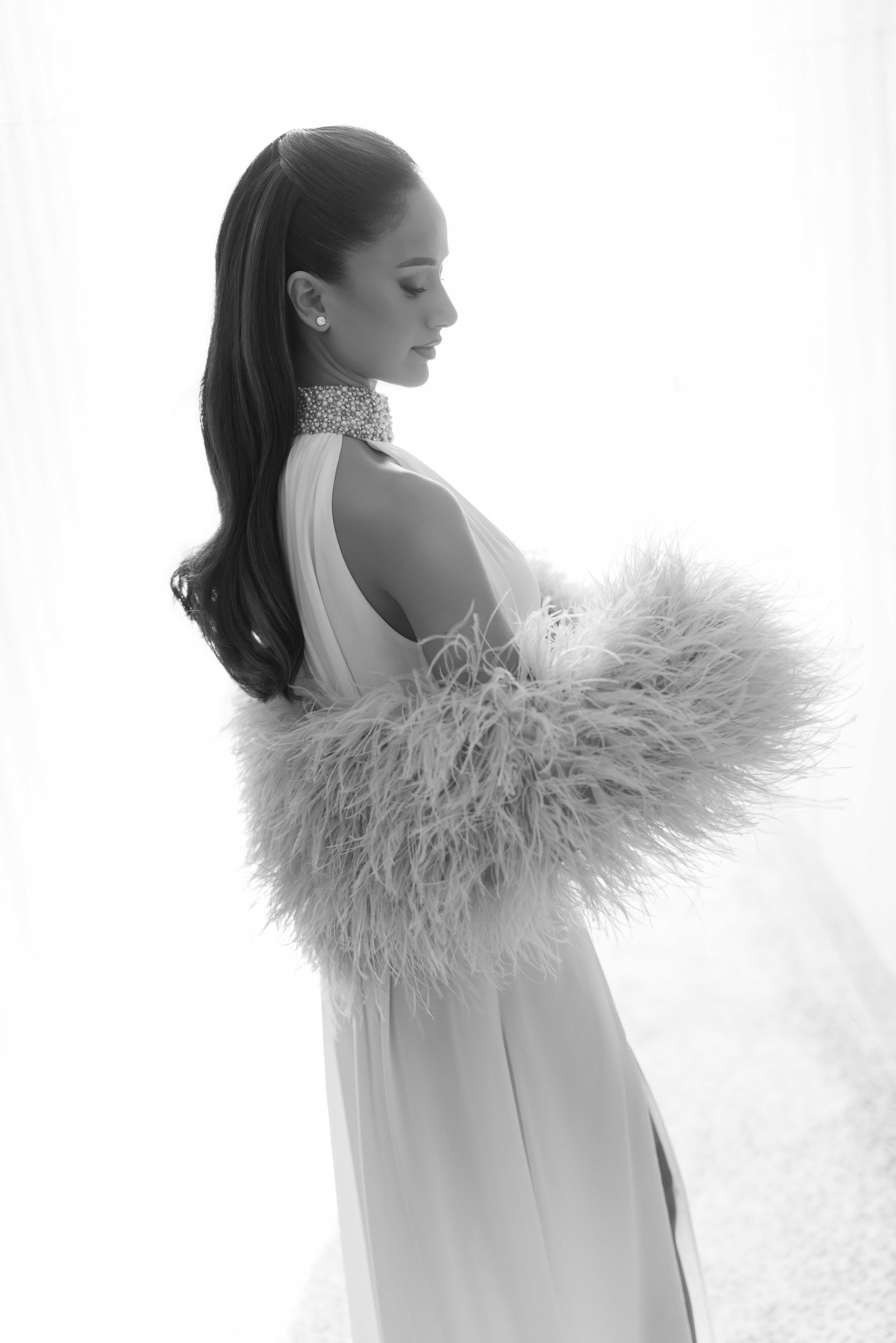 Black and white photo of elegant woman in flowing gown with feather wrap and jeweled choker necklace.