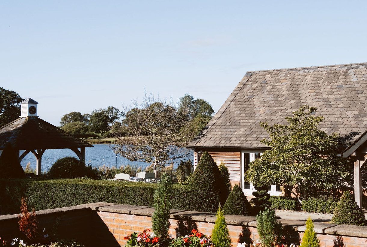 Sandhole Oak Barn wedding photography: the lake and a clock-topped gazebo beside a timber barn and gardens in the sun