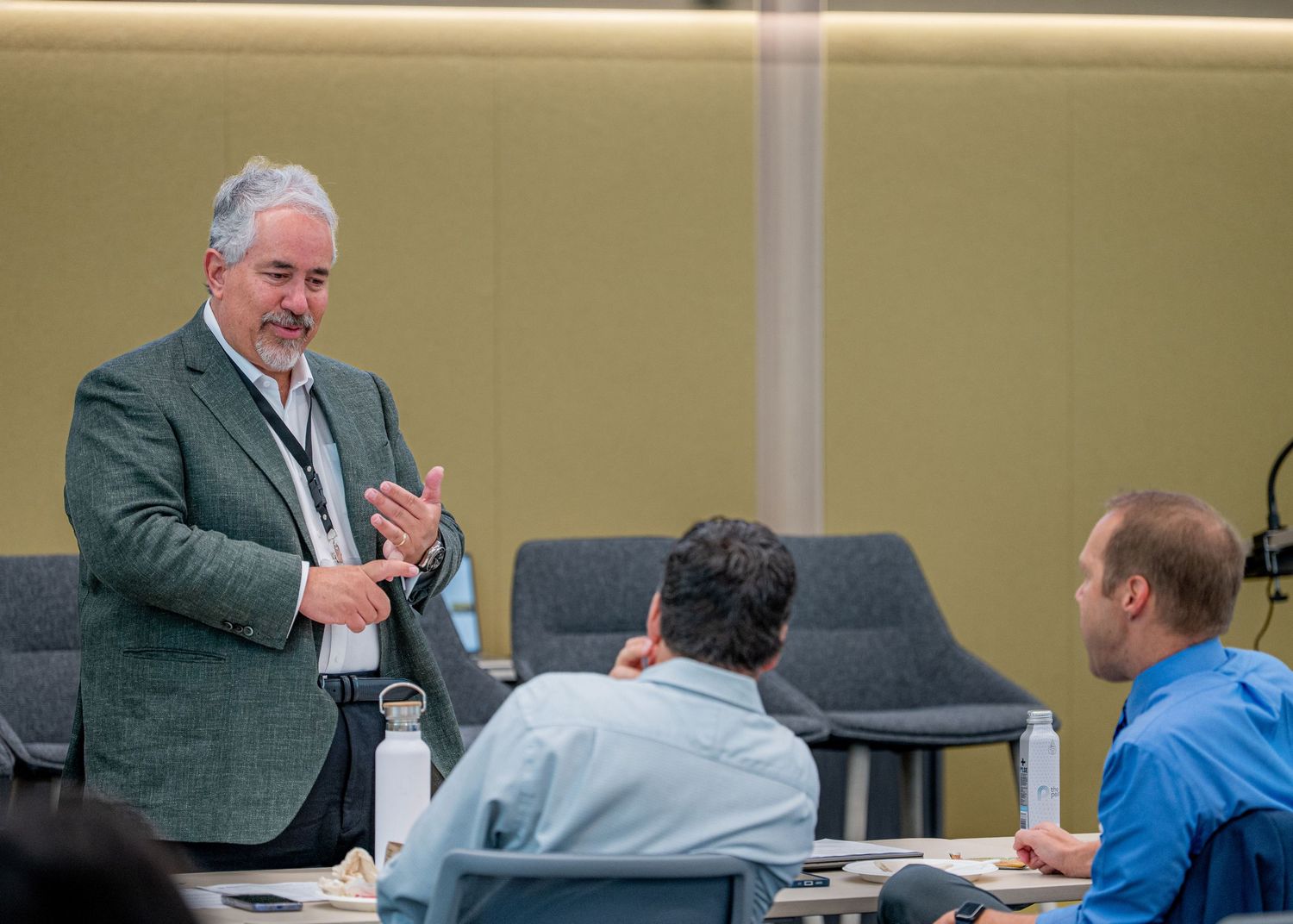 Professional speaker in green blazer engages seated attendees during a business meeting or workshop.