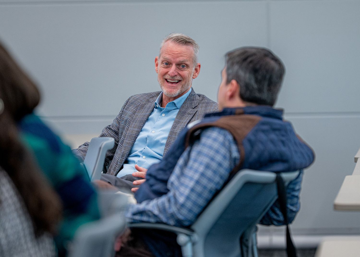 Two men engaged in a lively conversation while seated in chairs during a casual indoor meeting or discussion event.