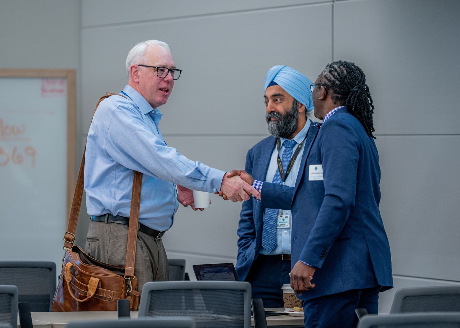 Three professionals shaking hands at a conference, including a man in a blue turban and suit.