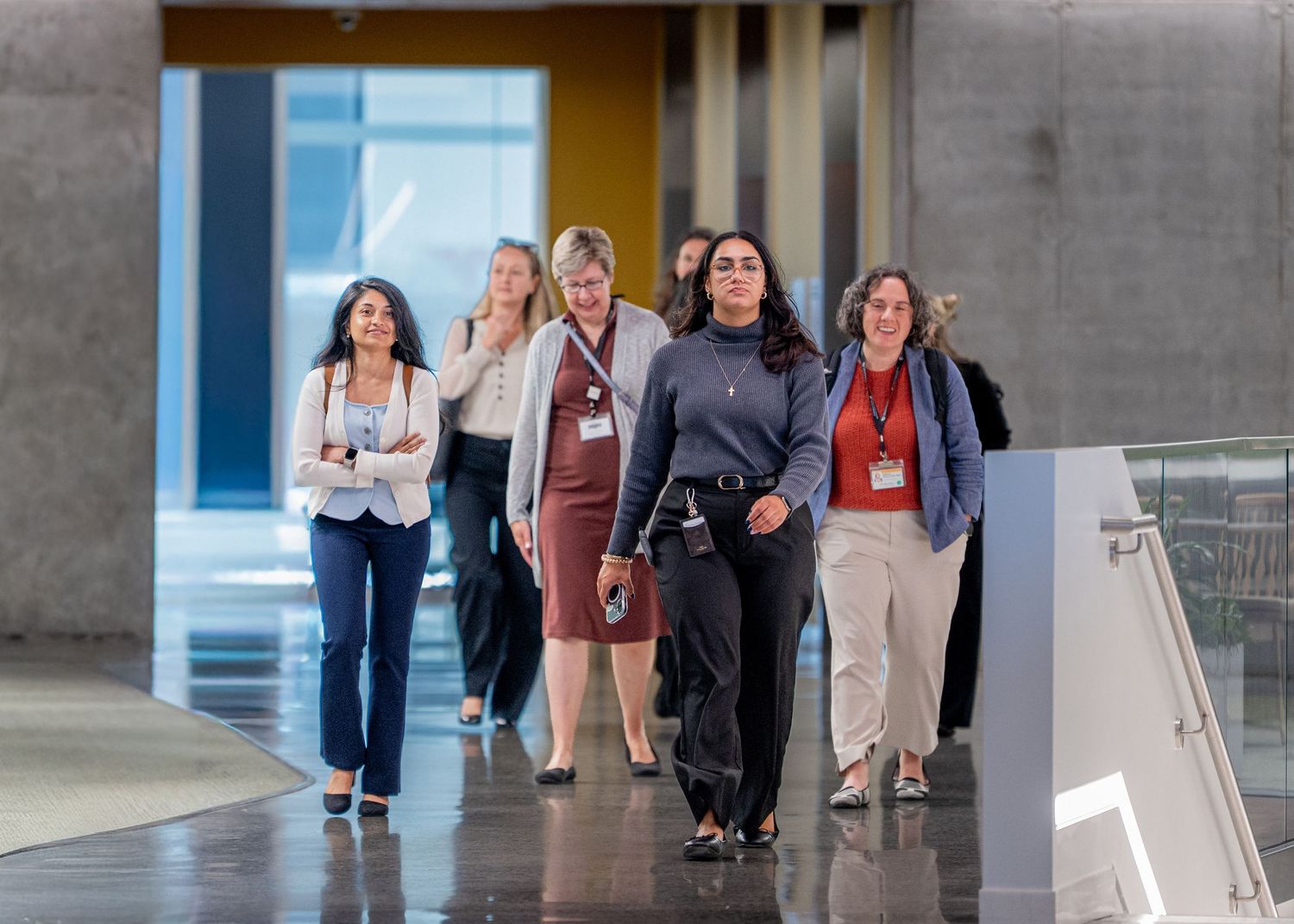 Group of professional women walking confidently through a modern building corridor during a business conference.