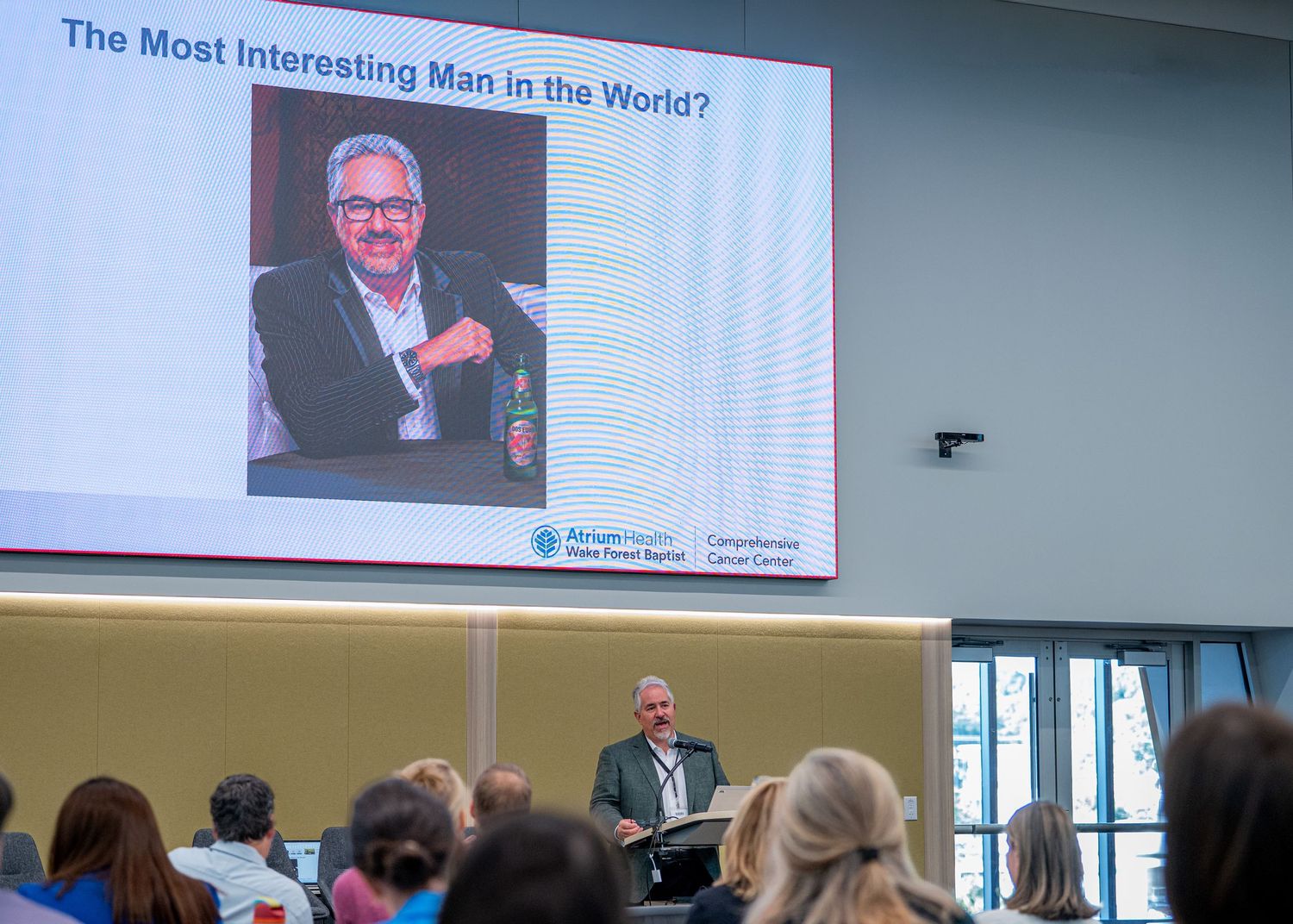 Speaker presents a slide titled The Most Interesting Man in the World at a medical conference with audience seated.