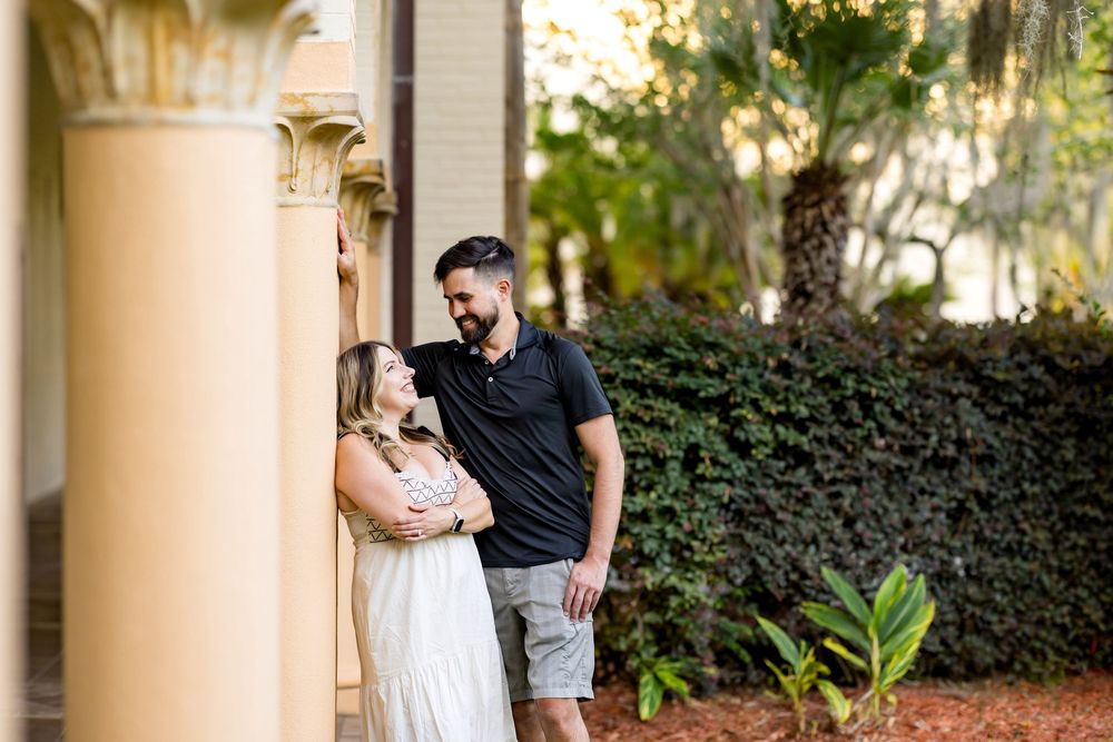 Couple sharing a romantic moment by a yellow column in a lush garden setting during golden hour.