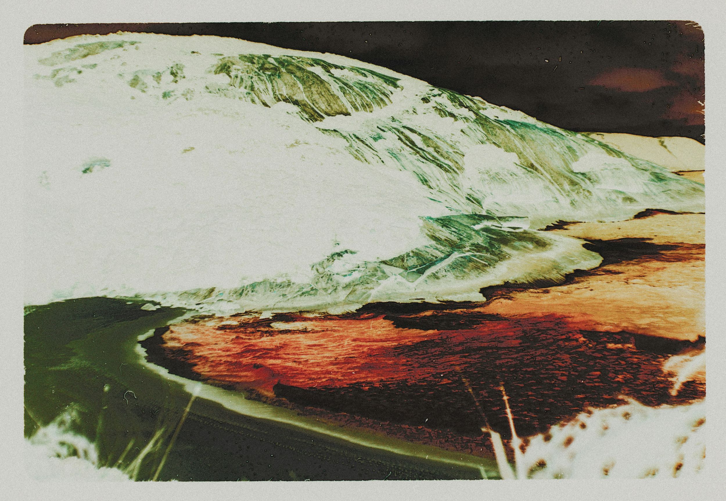 Close-up surreal photograph of melting ice and snow with green and brown tones on rocky terrain.