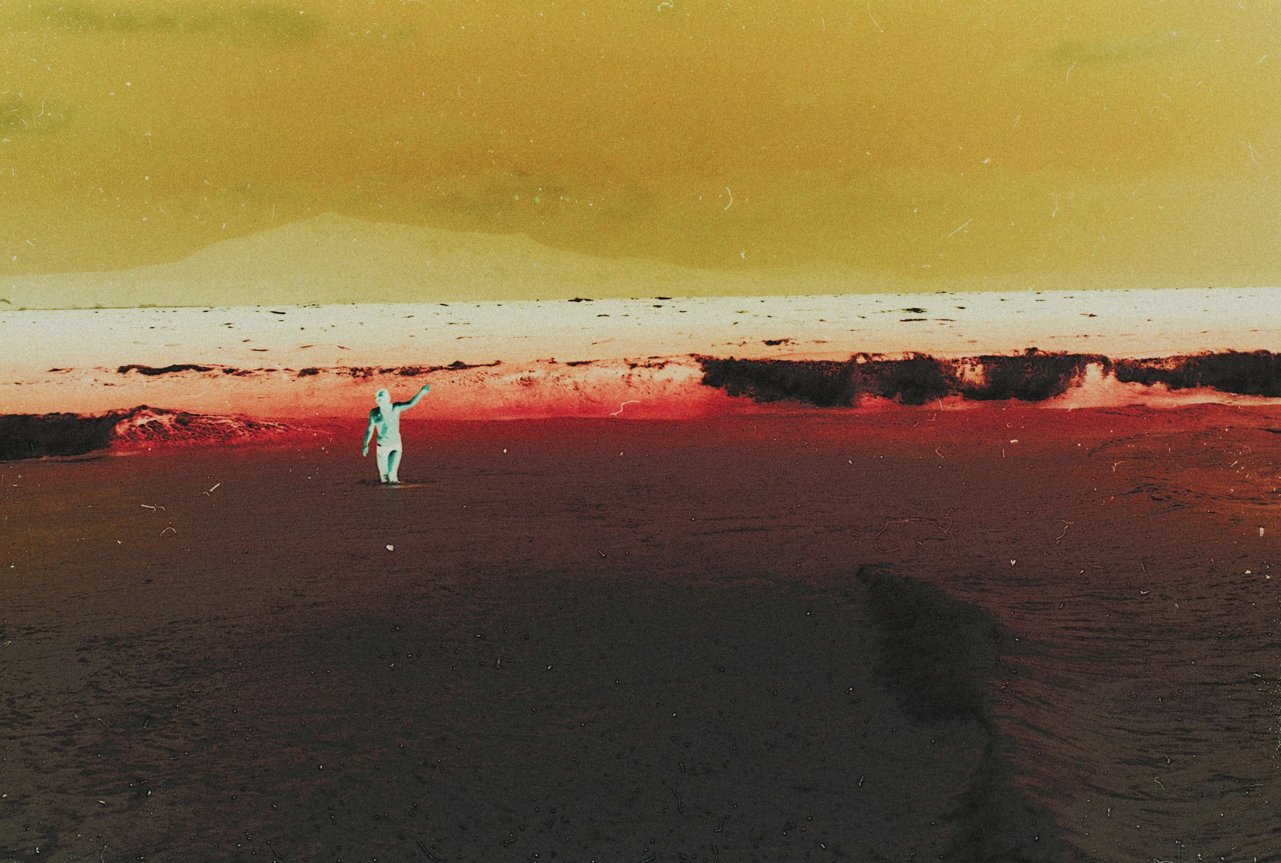 A lone figure stands on a vast red alien landscape under a yellow sky in this surreal infrared photograph.