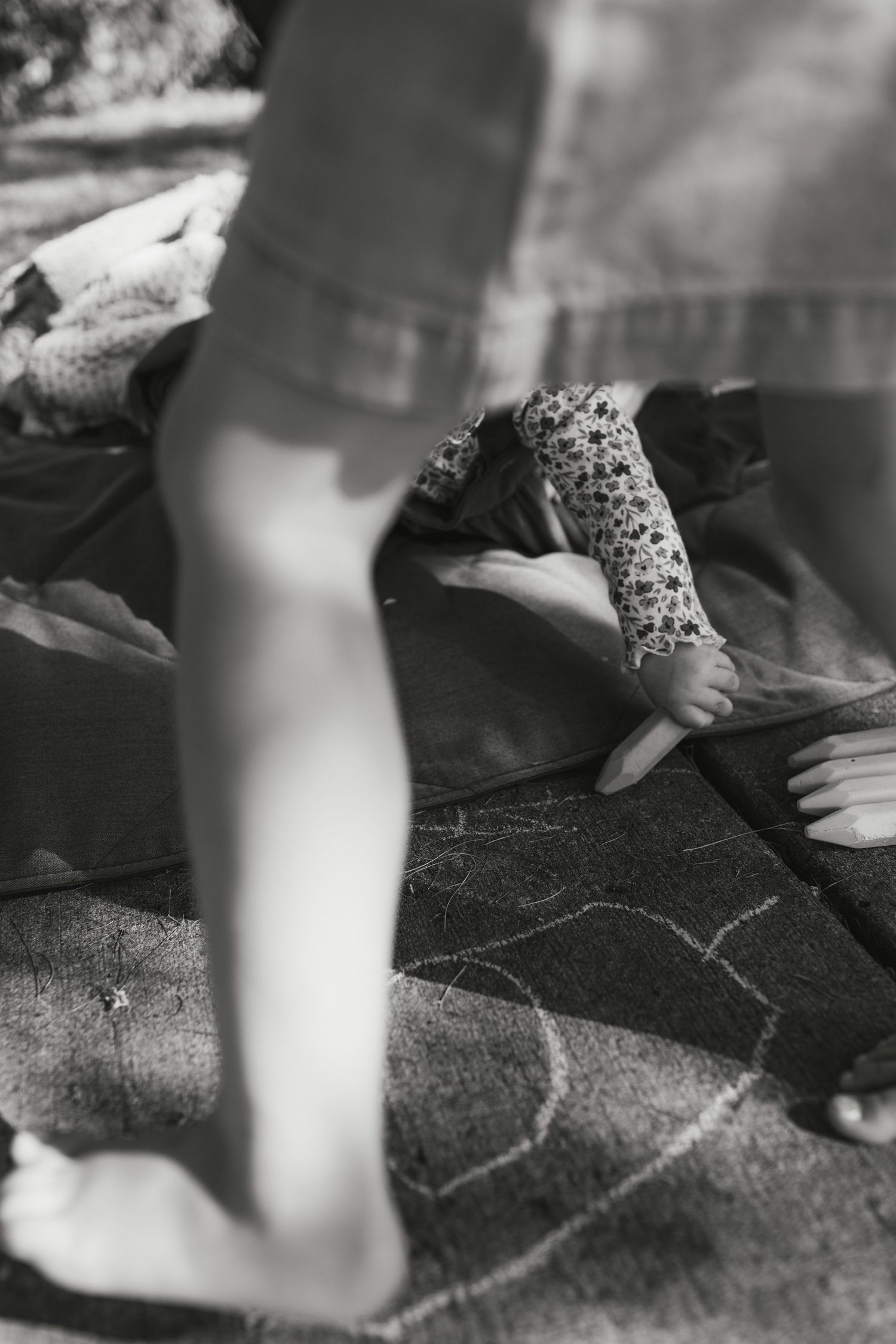 Black and white photo of children playing on a blanket outdoors, one wearing a decorative cast on their arm.