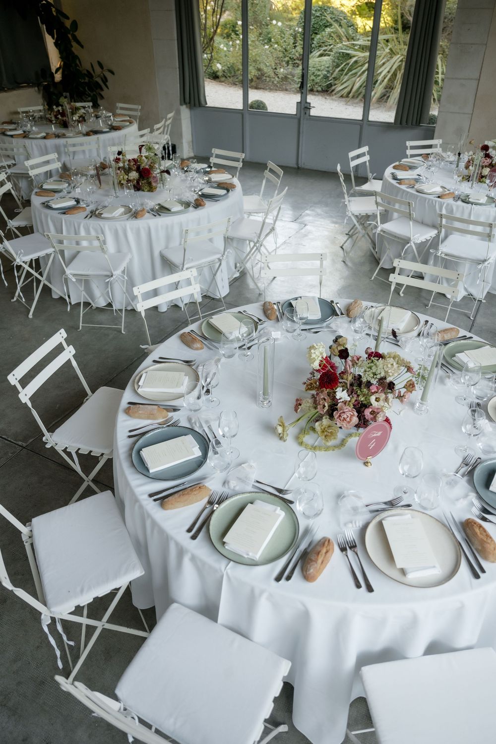 Elegant wedding reception venue with round tables draped in white linens, floral centerpieces, and white folding chairs.