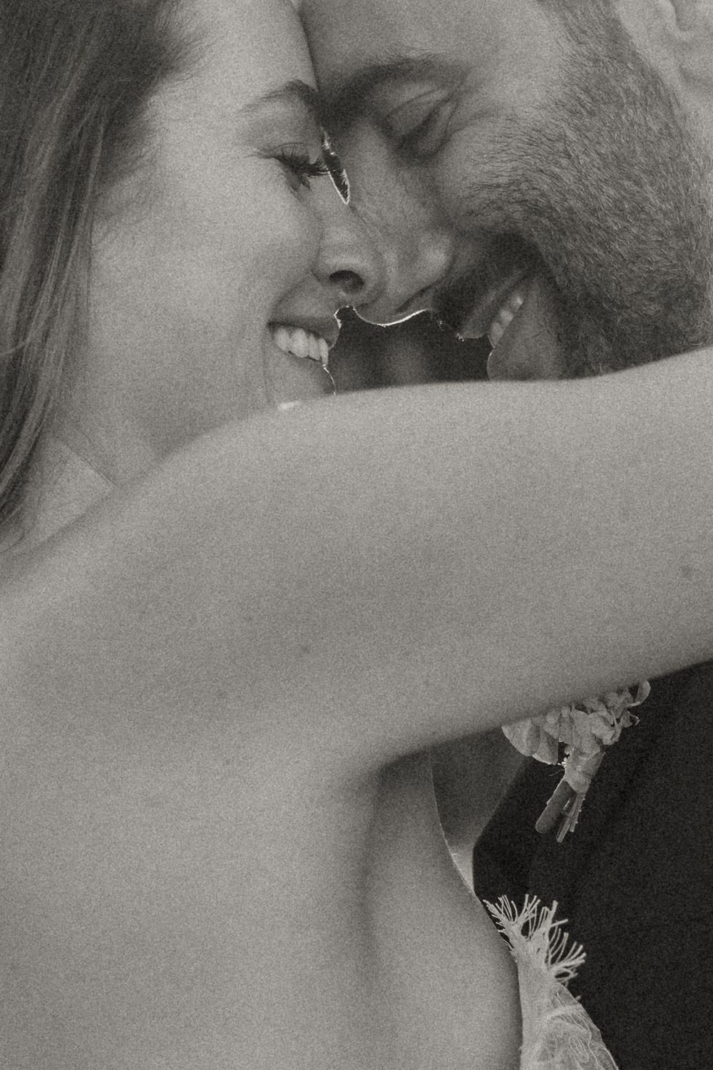 Black and white photo of a smiling bride and groom sharing an intimate moment, touching foreheads at their wedding.