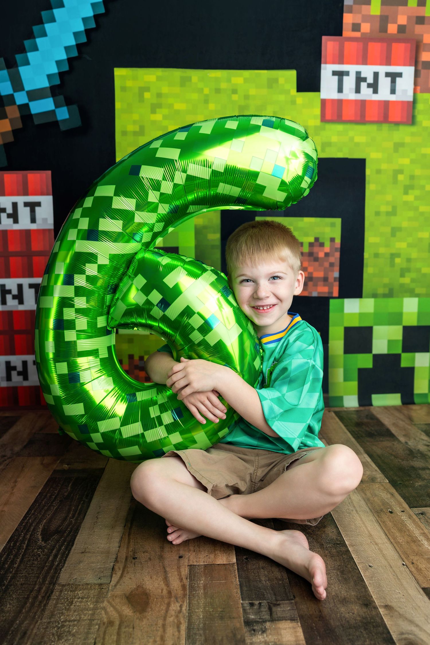 Smiling boy holding green number 6 balloon at Minecraft themed 6th birthday party with TNT block decorations.