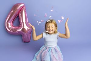 A joyful girl celebrates her 4th birthday with a pink number balloon and confetti on a purple background.
