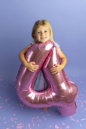 Smiling blonde girl hugging a large pink number 4 balloon on a purple background with confetti.