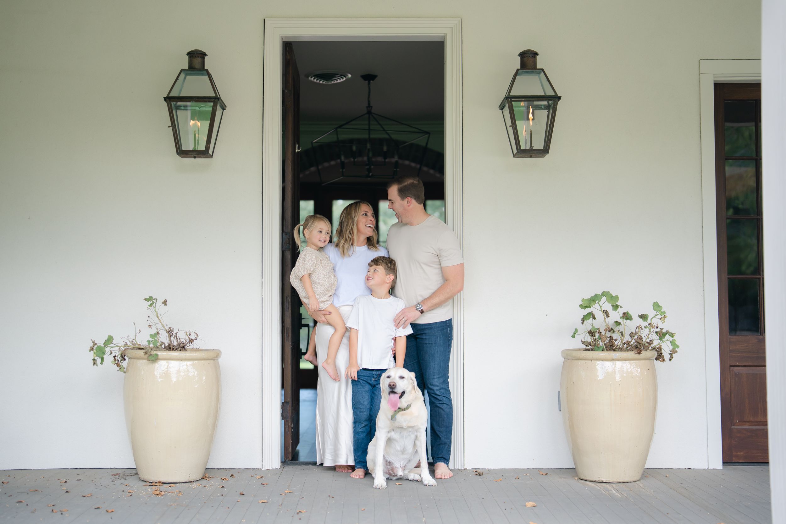 Family portrait with two children and white dog standing at front door of elegant home.