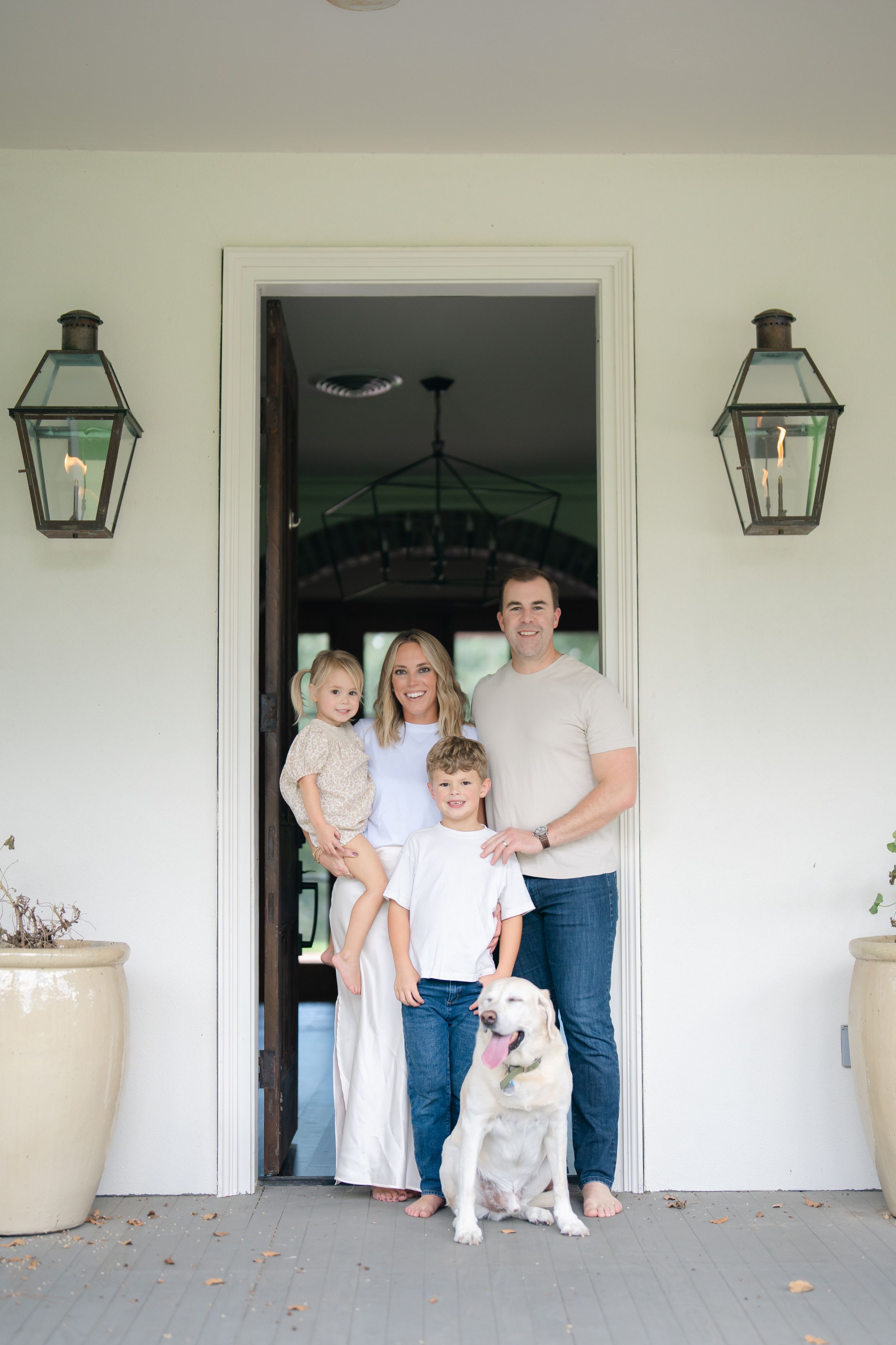 Family of four with white dog posing in front doorway of white home with gas lanterns.