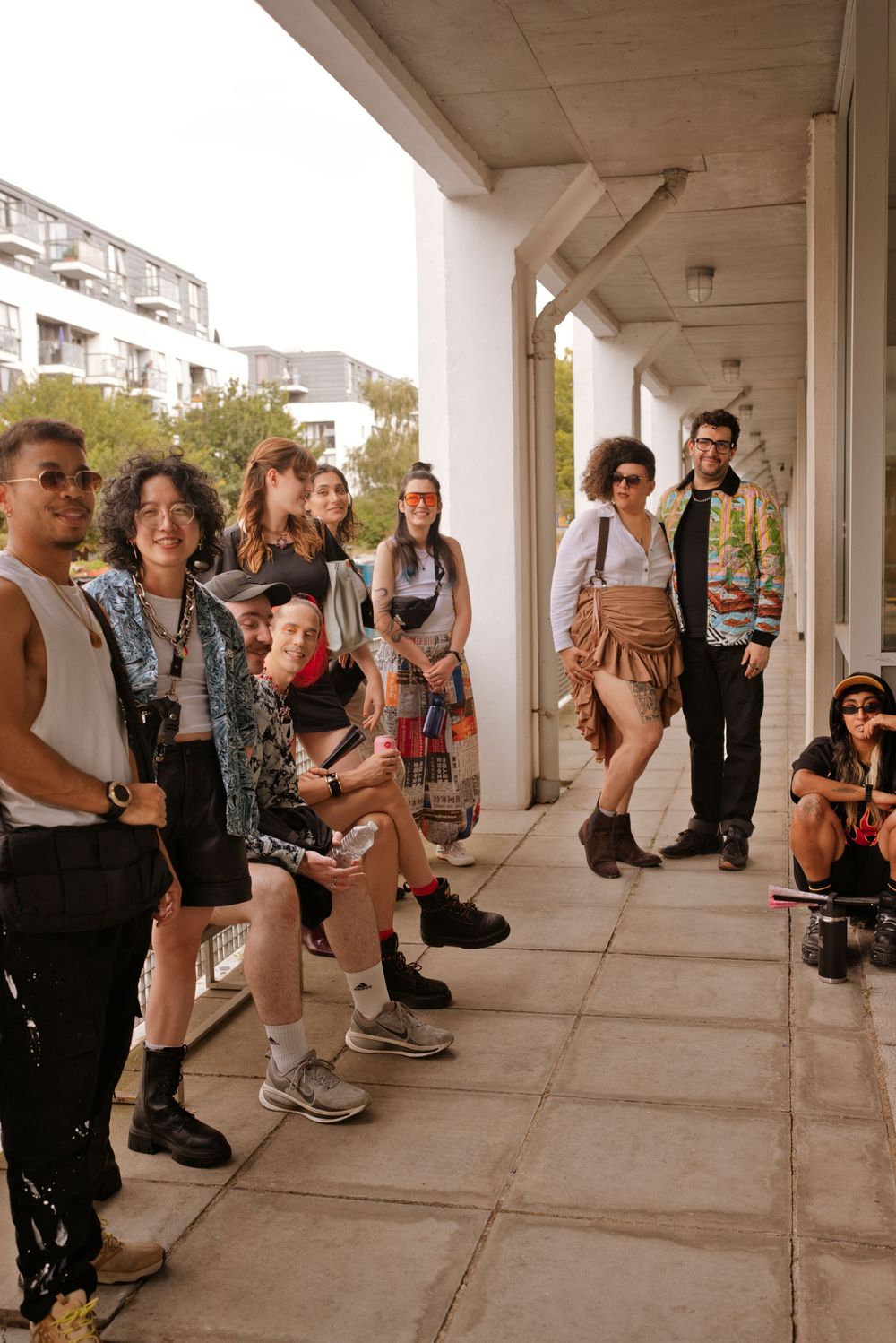 A diverse group of stylishly dressed young people gathered under a covered walkway at an outdoor urban event.