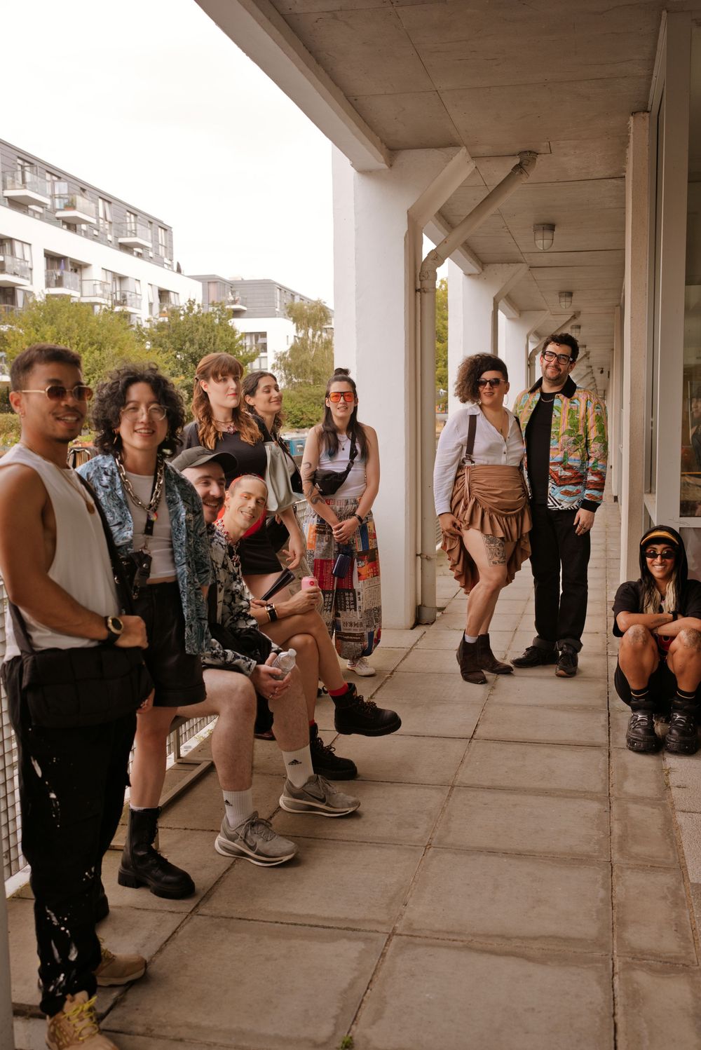 Diverse group of young adults in trendy outfits posing under a concrete walkway in an urban setting.