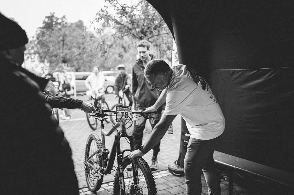 Black and white photo of a boy pushing a mountain bike through a tent entrance at an outdoor cycling event.