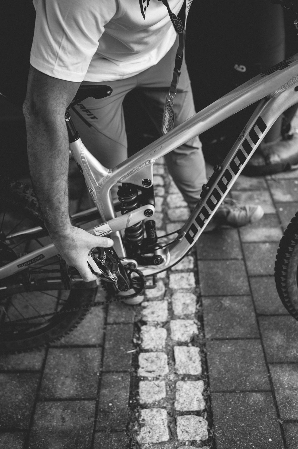 Man working on a mountain bike frame on cobblestone pavement, black and white photography.