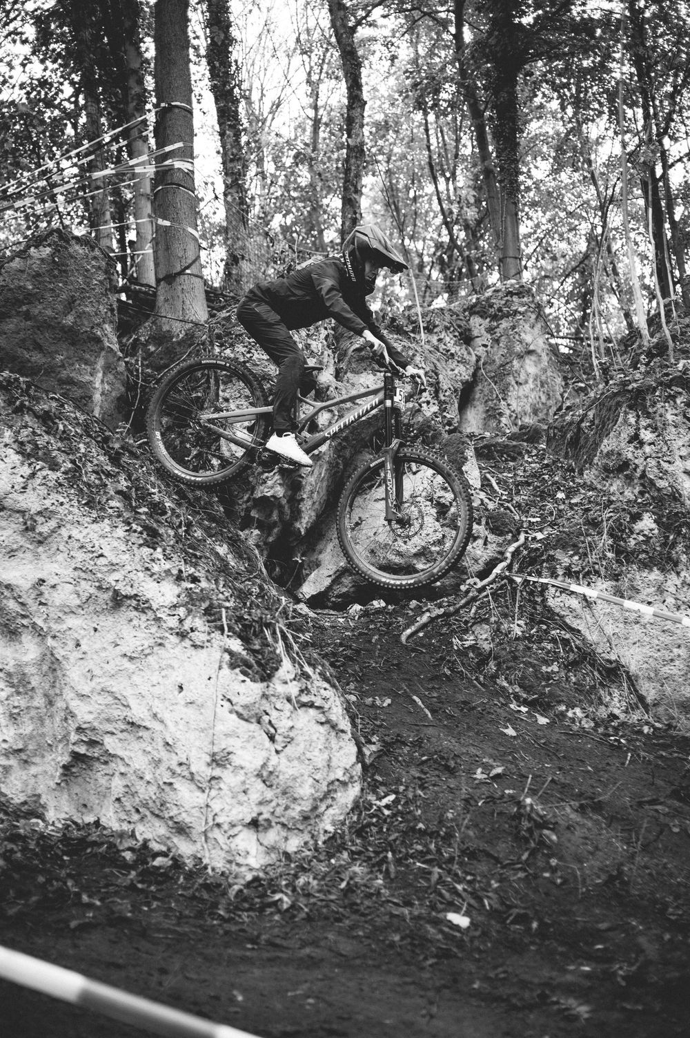 Black and white photo of a mountain biker navigating rocky terrain in a forest trail.