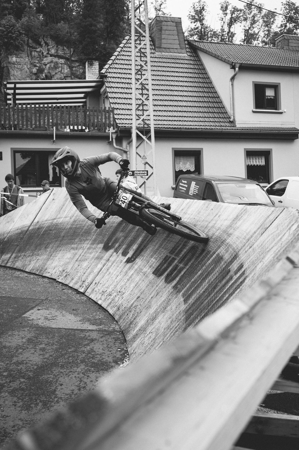 A cyclist performs a daring wall ride on a curved concrete ramp in a black and white urban setting.