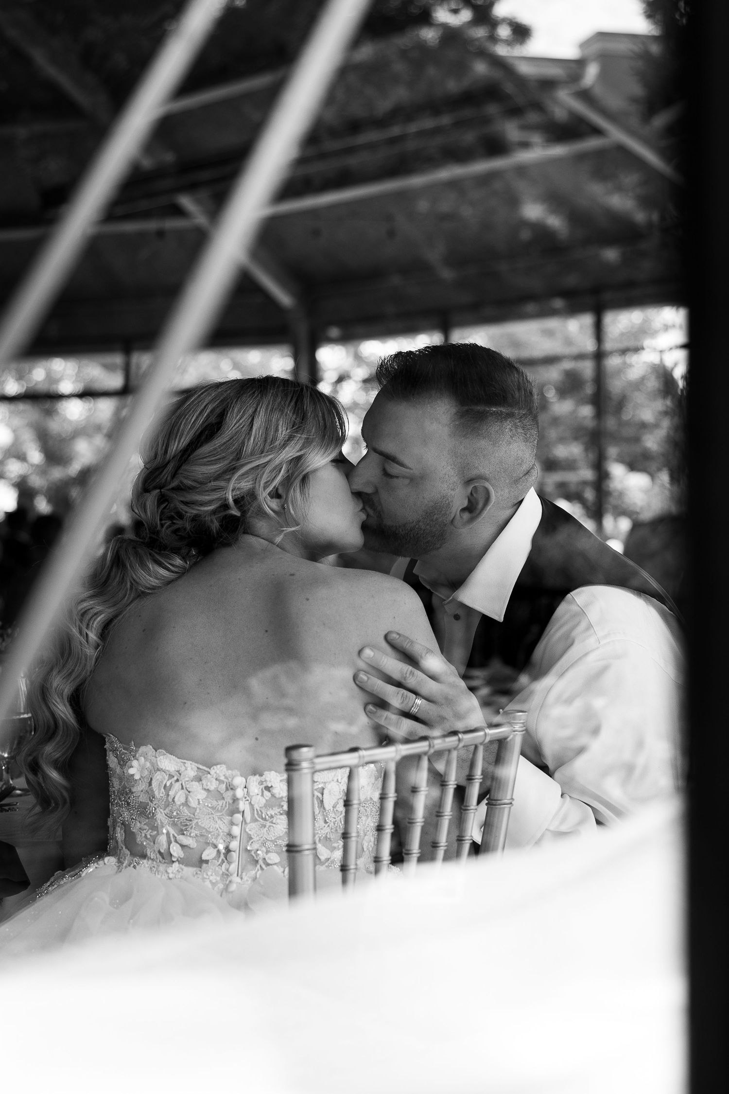 A romantic black and white wedding photograph showing a tender kiss between newlyweds under a covered venue.
