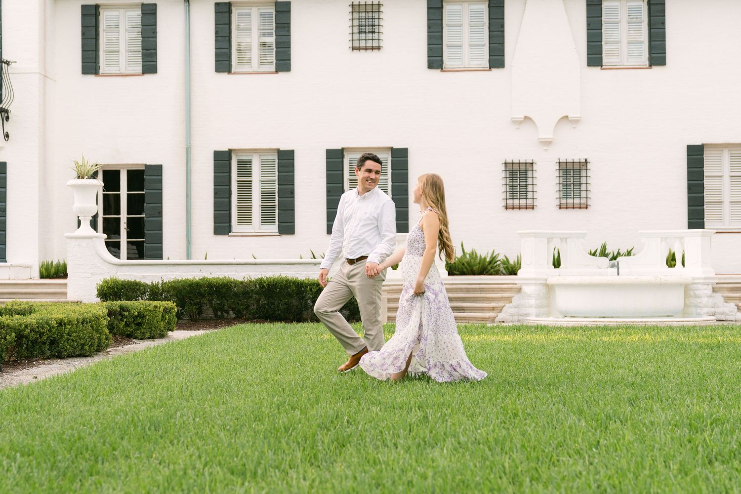 Engaged couple walking across the lawn in front of Crane Cottage on Jekyll Island, Georgia.
