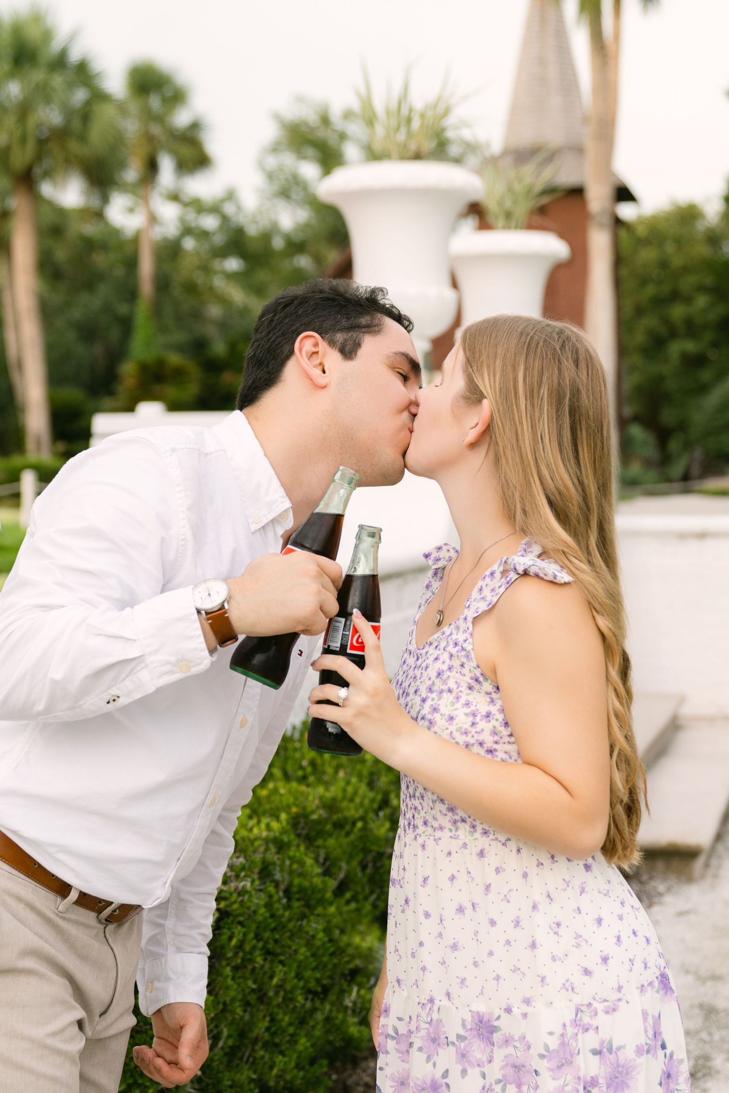 Engaged couple kissing while holding champagne flutes in the gardens of Crane Cottage on Jekyll Island.