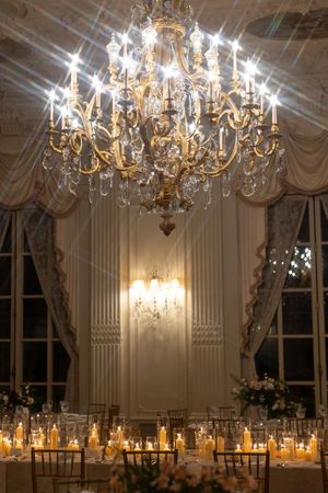 Grand crystal chandelier illuminates a romantic candlelit wedding reception with elegant table settings.