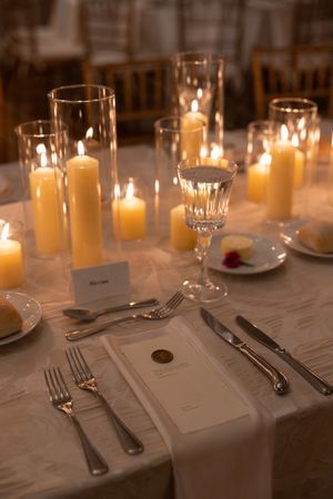 Elegant wedding reception table set with pillar candles in glass hurricanes, crystal stemware, and formal place settings.