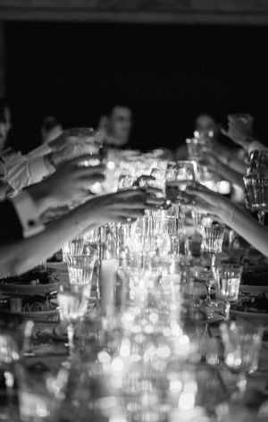 Black and white photo of guests raising crystal glasses in a toast at an elegant dinner party.