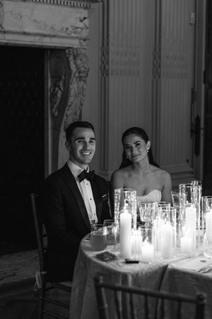 Bride and groom smile at sweetheart table adorned with pillar candles in black and white photo.