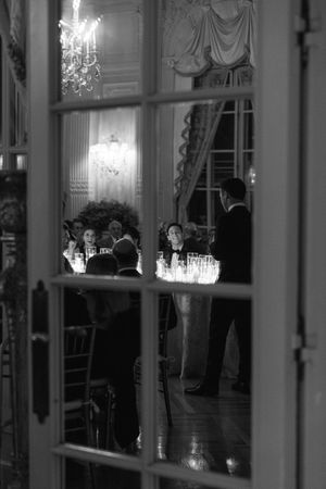 Elegant black and white photo of guests dining in a grand ballroom viewed through French doors.