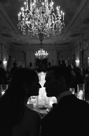 Romantic black and white wedding couple silhouette under crystal chandelier in elegant ballroom.