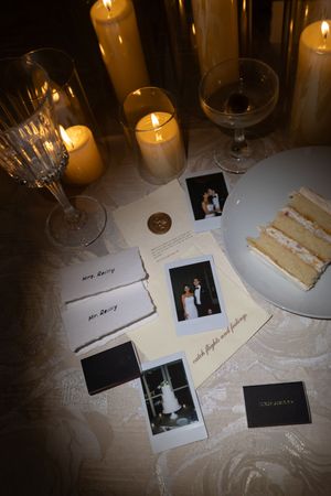 Wedding reception table with Polaroid photos, place cards, cake slice, candles, and crystal glassware in candlelight.