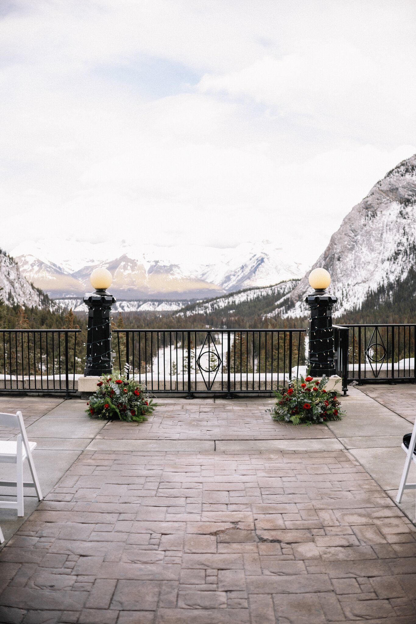 Empty outdoor ceremony terrace at the Fairmont Banff Springs framed by lamp posts, red rose florals and snowy mountains
