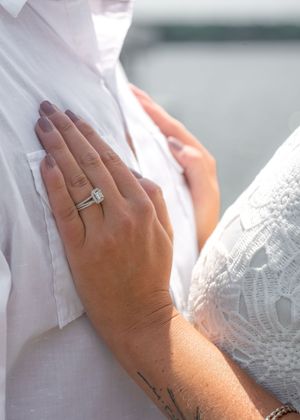 Close-up of a woman's hand wearing a diamond engagement ring and wedding band resting on a man's white shirt.