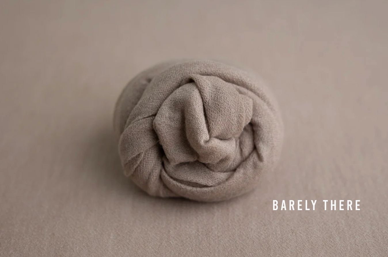 Soft beige newborn wrap rolled neatly on a neutral background, labeled Barely There, ideal for photography props.